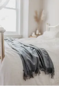 Cozy gray merino wool throw blanket detailed shot on bed, soft texture with elegant fringe.