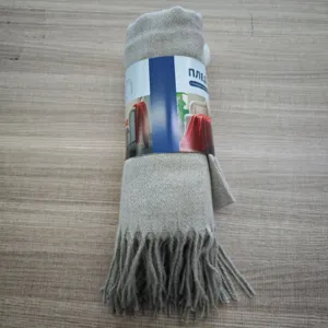 Dettaglio coperta con nappe in polyester, consistenza plaid arrotolato, tessuto grigio.