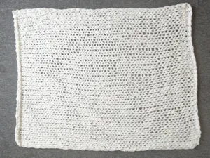Detailed close-up of white chunky knit blanket, showing thick handmade yarn texture clearly.