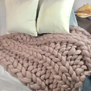 Detailed shot of a chunky knit blanket in soft dusty pink, thick handmade texture, bedroom decor.