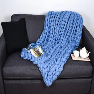 Detailed scene of a cozy blue chunky knit wool blanket draped over a modern dark gray sofa setup.