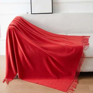 Morbida coperta rossa con frange su divano bianco, dettaglio di tessuto per la casa.