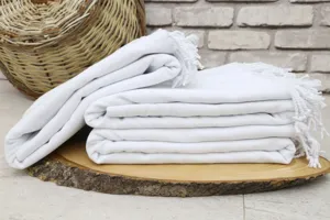 Close up detail of white Turkish beach towel with fringe texture stack on wood display.