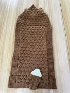 Close-up detail of brown knitted baby sleeping bag with textured popcorn pattern and hood.