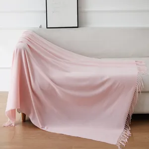 Vista dettagliata di morbida coperta rosa con frange drappeggiata su divano beige in casa.