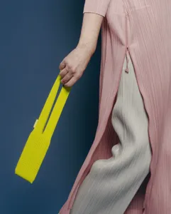 Detailed view of the stylish long knit bag and pleated fashion apparel in studio setting.