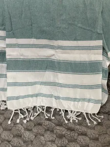 Close-up of Turkish beach towel detail, showing teal and white stripes with fringe tassels.
