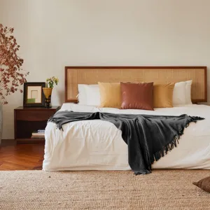 Dark grey knitted throw blanket with fringe detail in cozy bedroom setting, soft texture.