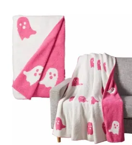 Cozy pink and white ghost blanket detail, soft fuzzy knit texture draped on grey sofa close up.