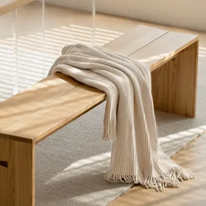 Close-up detail of a soft striped knitted throw blanket elegantly draped on wooden bench.