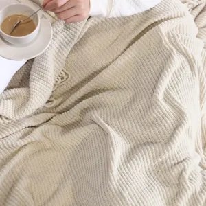 Detail shot of cozy beige knitted throw blanket texture, soft waffle pattern for home couch.