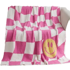 Pink and white checkerboard knit throw blanket with cute yellow smiley face for sofa decor.
