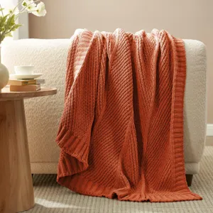 Cozy knitted throw blanket detail shot, featuring textured diagonal stripes in vibrant rust orange.