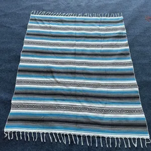 Mexican woven blanket with geometric stripes and fringe boho style throw for beach and picnic.