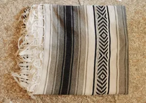 Woven Mexican blanket detail showing black and white geometric stripes and delicate fringe tassels.