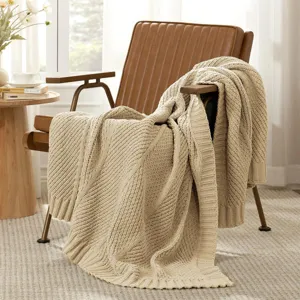 Beige knitted throw blanket draped over leather armchair, cozy home decor and soft texture detail.