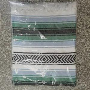 Woven Mexican blanket detail view showing geometric stripes and fringe design, soft cotton fabric.