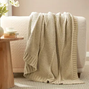 Cozy beige knitted throw blanket with diagonal stripe texture draped on modern living room sofa.