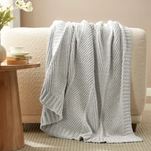 Detailed view of cozy grey knitted blanket draped on beige sofa with home decor setup.