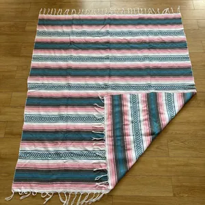 Woven Mexican blanket with geometric stripes, pink teal colorway, fringes, and soft texture.