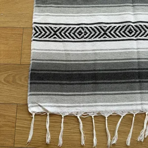 Close-up detail of a woven Mexican blanket with black, grey, white stripes and decorative fringe.