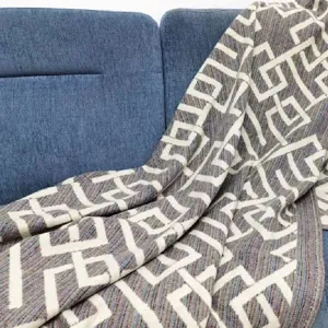 Gedetailleerde opname van een zachte geweven jacquard deken met geometrisch patroon op blauwe bank.