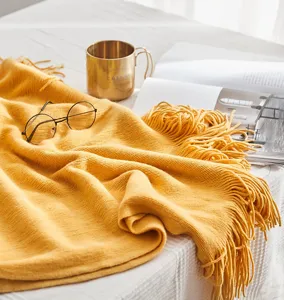 Cozy yellow knitted throw blanket detail with fringe tassels, lifestyle bedroom home decor scene close up.