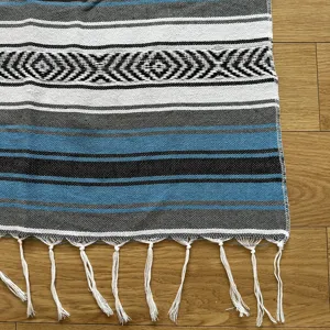 Close-up detail of woven striped Mexican blanket texture with decorative fringe tassels.