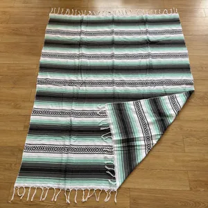 Detailed shot of a woven Mexican blanket featuring mint green, black, white stripes and fringe.