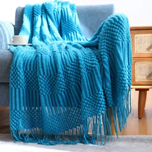 Close-up view of bright blue knitted throw blanket with geometric texture and elegant fringe.