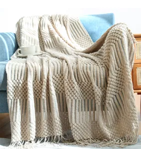Detailed view of a cozy beige knitted throw blanket with tassels draped on a modern blue sofa.