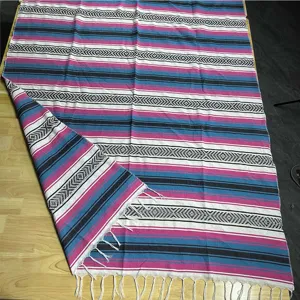 Detailed view of woven Mexican blanket with colorful stripes, diamond patterns and soft fringes.