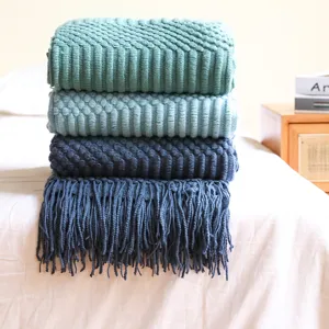 Detailed view of stacked knitted blankets with fringe, soft texture for cozy home decor.