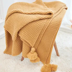 Detailed close-up of a cozy yellow knitted throw blanket featuring elegant tassels and soft texture.