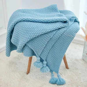 Detailed view of a soft blue knitted throw blanket with tassels for cozy home decor.