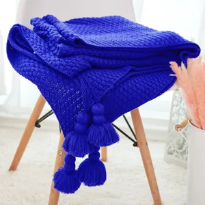 Royal blue knitted throw blanket with large tassel pom poms, cozy sofa couch cover decor.