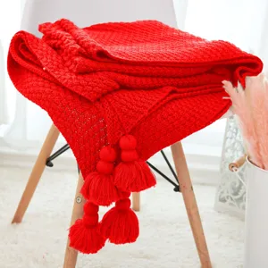 Red knitted throw blanket with tassels and pompom, cozy sofa cover for summer air conditioning.