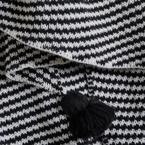 Close-up detail of black and white knitted blanket with tassel pom-pom home decor texture.