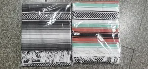 Vue détaillée de couvertures mexicaines tissées à rayures colorées et franges sous film plastique.