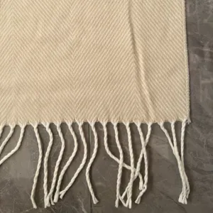 Close-up detail view of woven herringbone pattern throw blanket with soft fringe trim.
