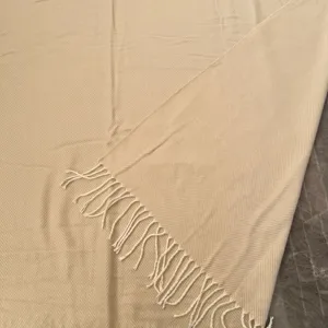 Detail shot of beige herringbone woven throw blanket with fringe, cozy home textile decor.