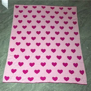 Detailed shot of the pink knit blanket featuring repeating dark pink heart patterns close up.