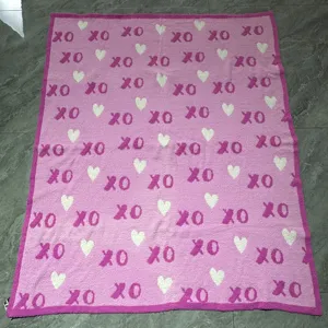 Pink knitted throw blanket with white hearts and XO patterns, soft cozy fuzzy material for gift.