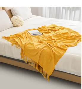 Detailed view of the cozy yellow knitted throw blanket with tassels draped elegantly on the bed.