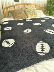 Accogliente coperta in maglia grigio scuro con motivi di football bianchi, dettaglio texture.