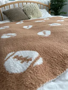 Vista ravvicinata di dettaglio della comoda coperta in maglia marrone con motivo sportivo bianco.
