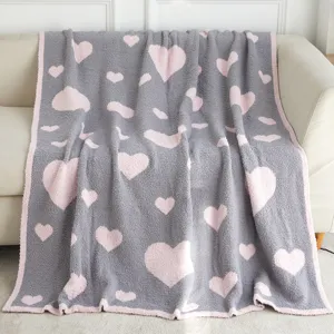 Cozy grey plush knit blanket with pink heart pattern draped softly over a modern sofa.
