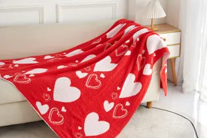 Cozy red heart pattern microfiber blanket draped on beige sofa in warm room detail scene.