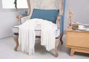 Nahaufnahme der weißen gestrickten Wohndecke, anmutig auf einem Vintage-Sessel drapiert.
