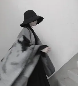 Detailed view of the black and gray tie-dye wool-feel cape shawl worn by the model on stairs.